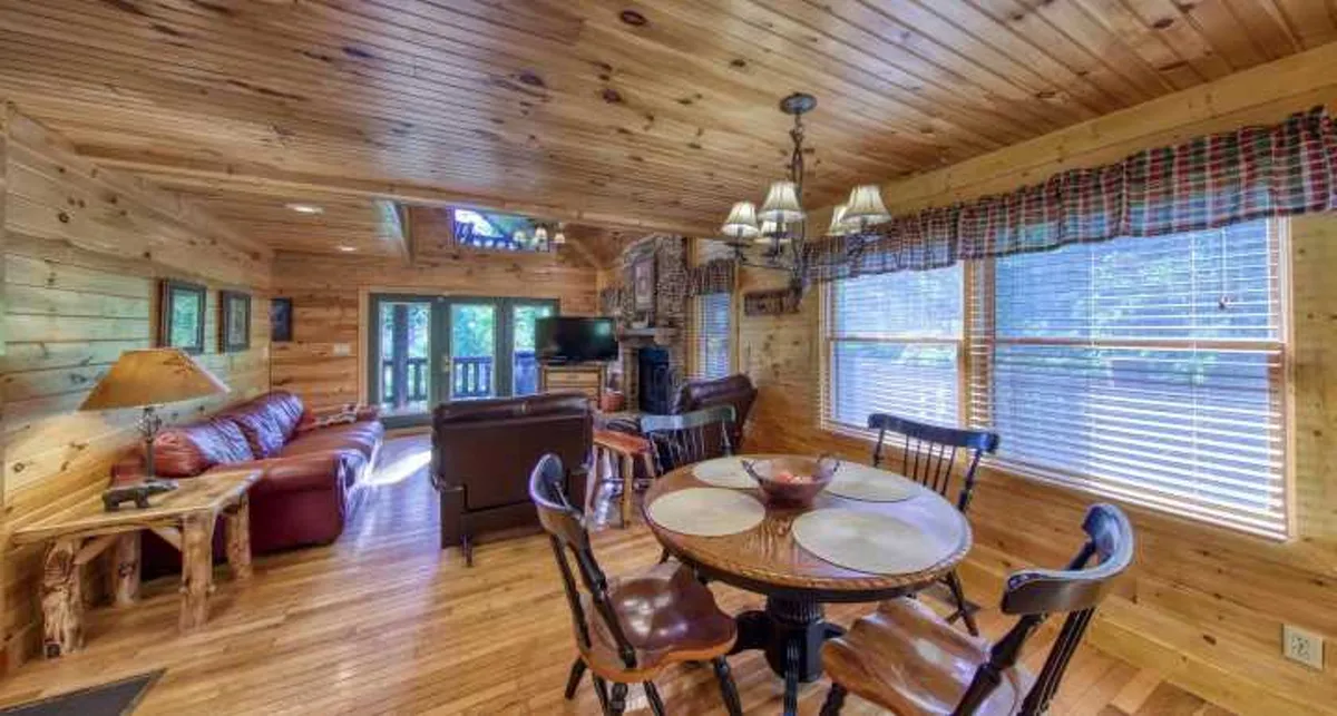 A sunlit interior space featuring a wooden dining table, leather sofa, and expansive windows that frame mountain views. The area invites family meals, game nights, or quiet mornings soaking up the scenery.