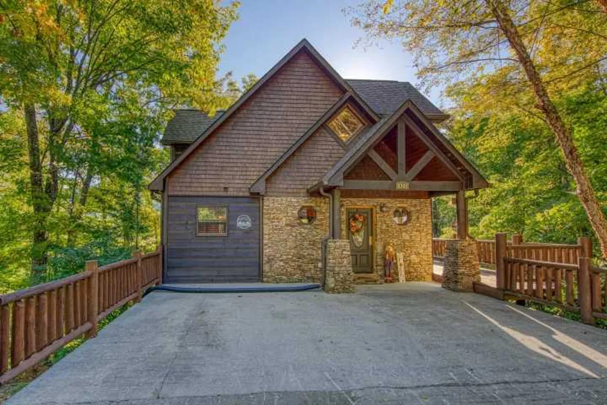 This image features a prominent stone-front entryway with wooden railings, large windows, and lush surrounding trees. The entry is framed by natural wood and stone textures, embodying the welcoming and rustic charm of the cabin as guests arrive.