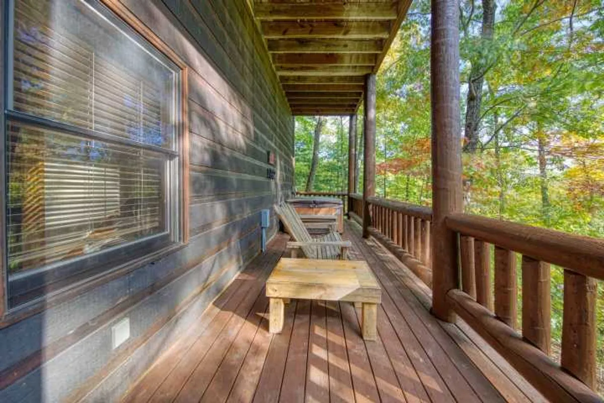 A spacious wooden deck outfitted with Adirondack chairs overlooks a lush, wooded landscape. The deck invites relaxation and provides the perfect spot to listen to birdsong or watch the sunset, with trees enveloping the area in tranquility.